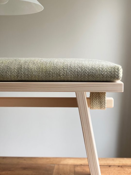 Seitenansicht der Sitzbank aus hellem Holz mit Wollkissen.