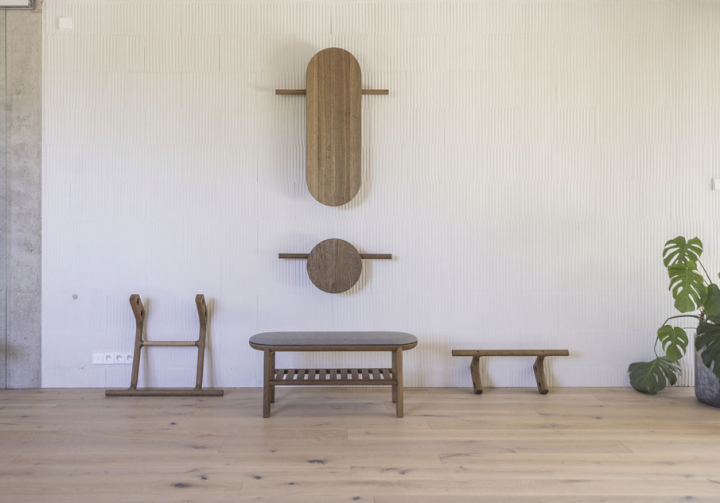 Holzelemente der SANA-Kollektion an der Wand arrangiert; Bank und Zubehör davor.