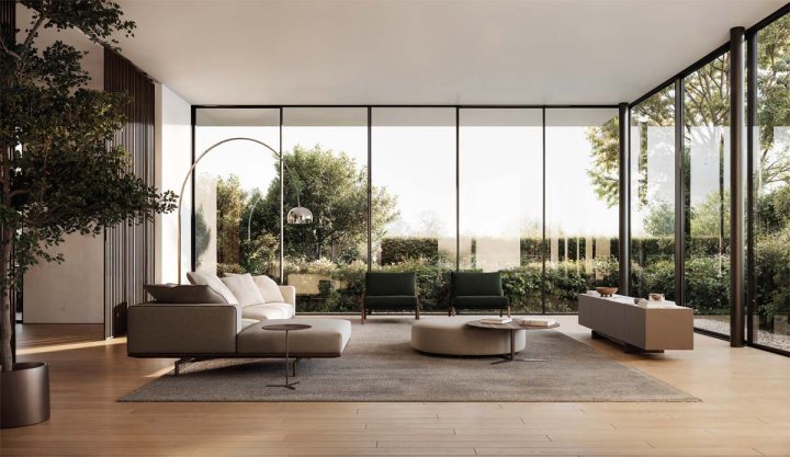 Modernes Wohnzimmer mit grossen Glasfronten, hellen Sofas, zwei grünen Sesseln, rundem Couchtisch und Blick ins Grüne