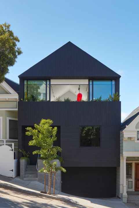 Reihenmittelhaus mit dunkler Holzfassade. im Fenster sieht man markante rote Leuchten.