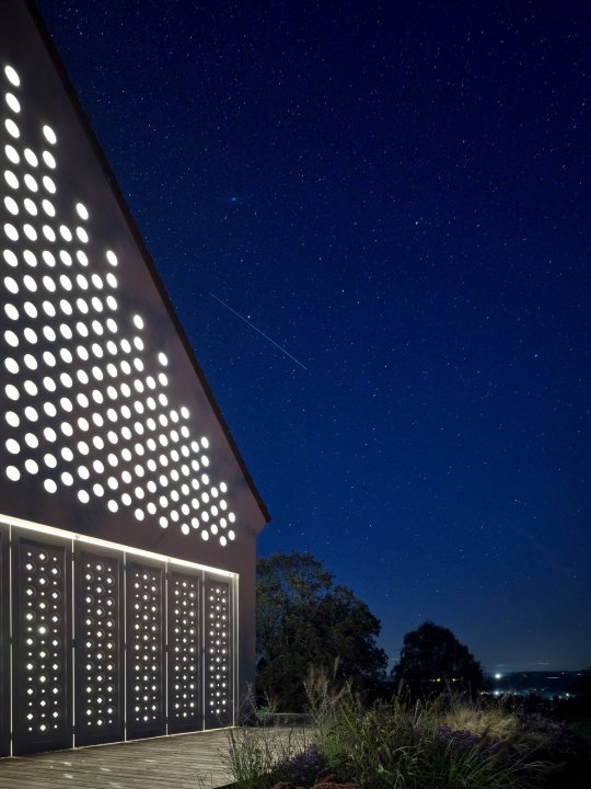 Moderne weisse Holzfassade mit durchlässigem Muster unter einem Sternenhimmel.