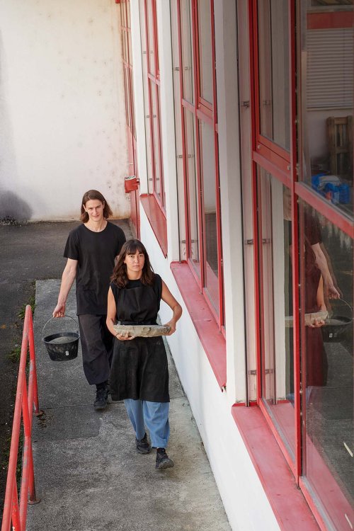Ein Foto des Duos. SI laufen durch einen schmalen Gang und tragen schwarze Schürzen.