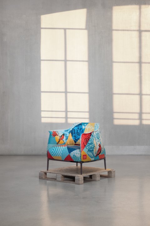 Schräg von hinten fotografierter, farbig bedruckter Armchair auf einer Holzpalette in einem hellen Raum mit grossen Fensterschatten an der Wand