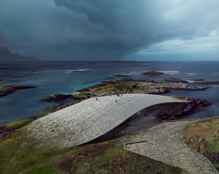 Dramatische Luftaufnahme von „The Whale“ an der Küste von Andenes. Das Gebäude mit seinem steinernen, begehbaren Dach schmiegt sich wie ein riesiger Walrücken an die felsige Küste, während sich im Hintergrund ein dunkler, stürmischer Himmel über dem Nordmeer zusammenzieht.