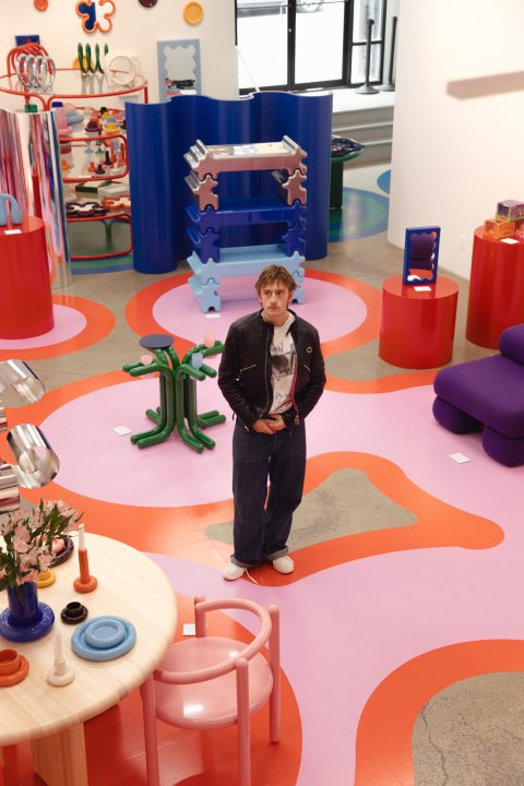 Gustaf Westman steht in einer farbenfrohen Ausstellungsfläche mit pinkem Boden, umgeben von bunten Designobjekten und Möbeln.