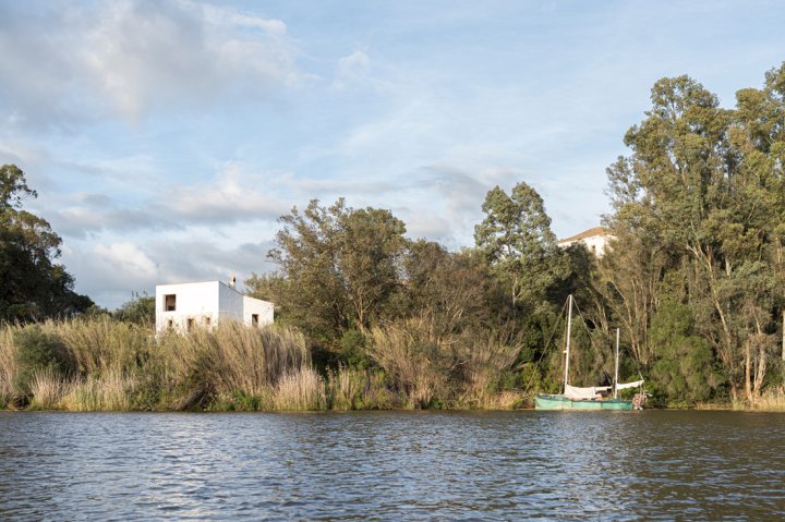 Haus Stone and Water am Ufer des Guadiana mit Boot vor Flusslandschaft mit Bäumen und Schilf